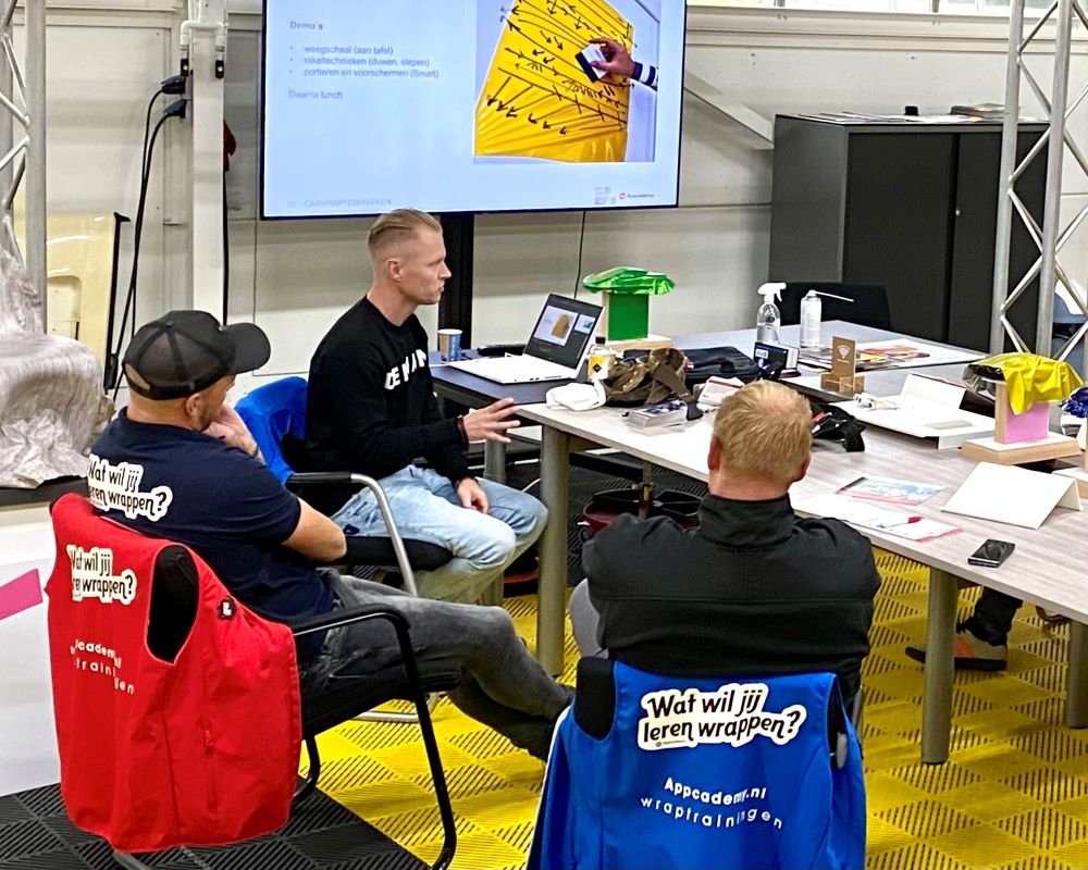 Trainer geeft aan tafel instructies aan cursisten met behulp van een power point presentatie tijdens de Appcademy signmaker opleiding cursus